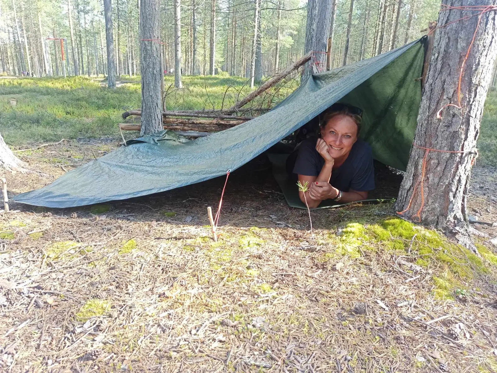 Nauczycielka pod schronieniem z tarpu rozstawionym między sosnami podczas zajęć outdoorowych